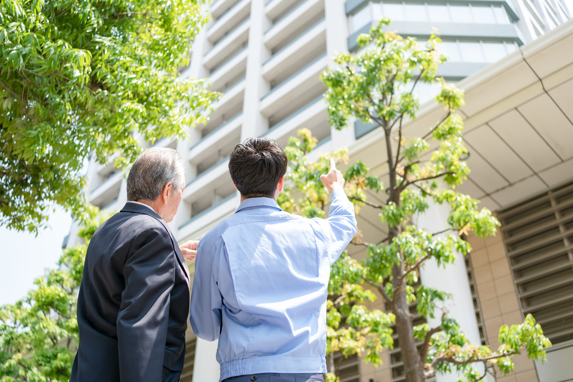 マンション管理・経営についてオーナーとマンションの下で話している賃貸管理社員